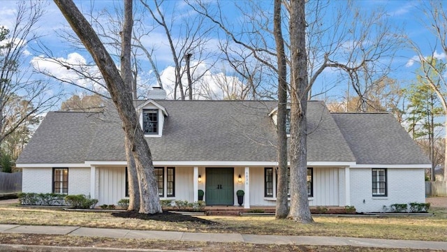 cape cod home featuring brick siding, roof with shingles, a chimney, a porch, and a front yard