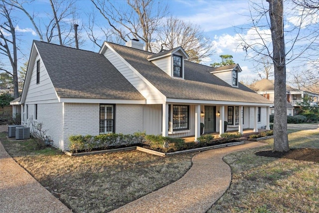 cape cod house with brick siding, a chimney, a shingled roof, covered porch, and central AC unit