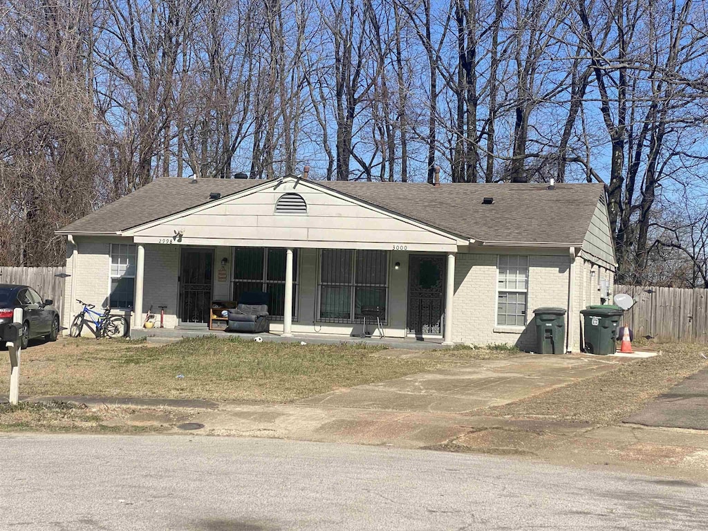 bungalow-style house with covered porch, brick siding, fence, and roof with shingles