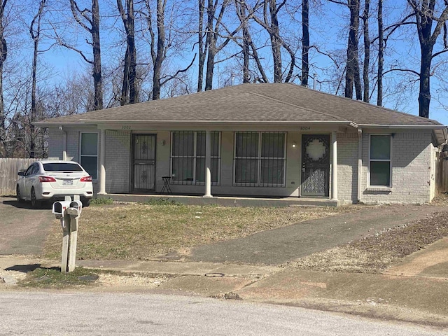 view of front of property featuring a shingled roof, brick siding, and fence