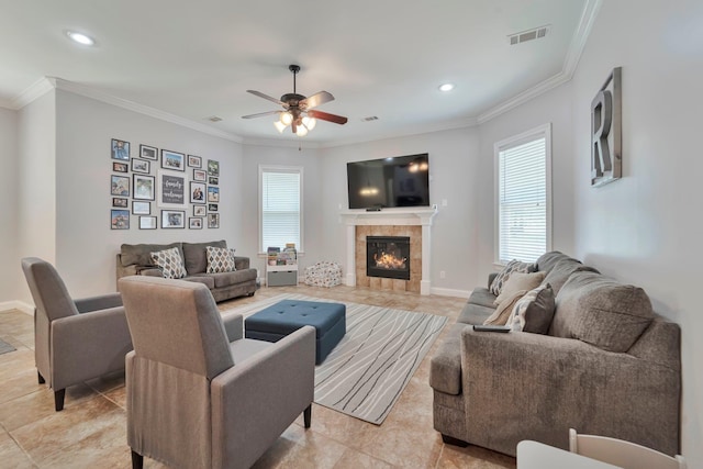 living room featuring baseboards, a tiled fireplace, visible vents, and crown molding