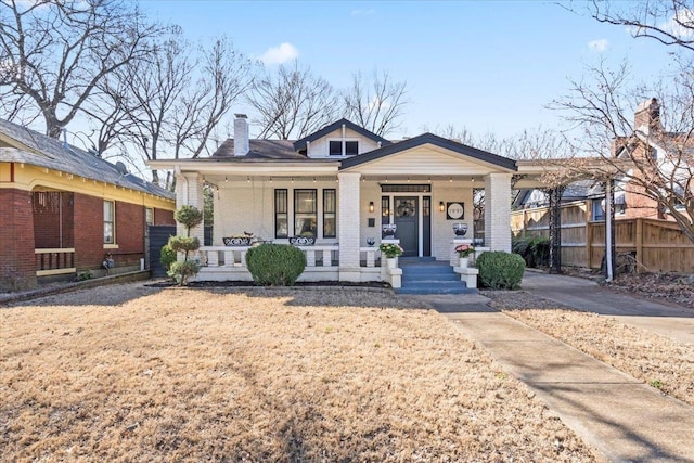 bungalow-style home featuring covered porch, a chimney, fence, and brick siding