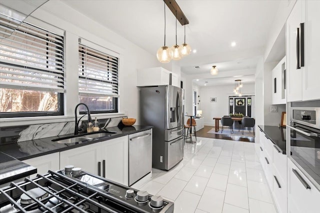 kitchen with white cabinets, dark countertops, appliances with stainless steel finishes, a sink, and a wealth of natural light