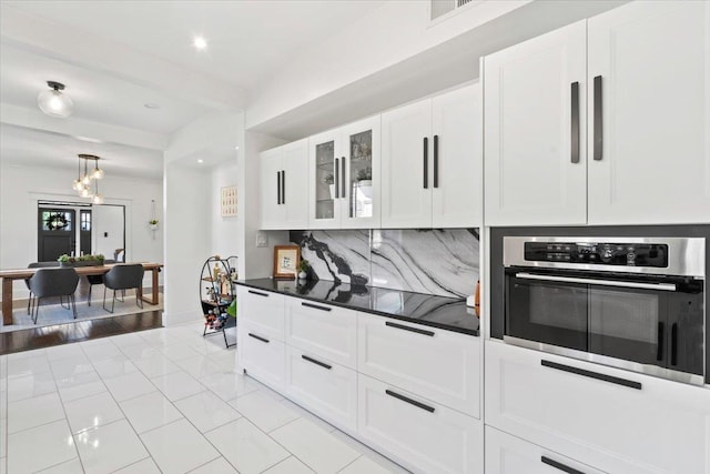 kitchen with beam ceiling, dark countertops, decorative backsplash, white cabinetry, and oven