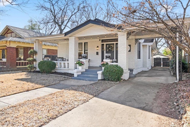 bungalow-style home featuring covered porch, brick siding, a chimney, and an outdoor structure