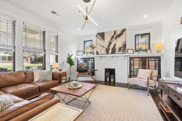 living room featuring a brick fireplace, visible vents, crown molding, and wood finished floors