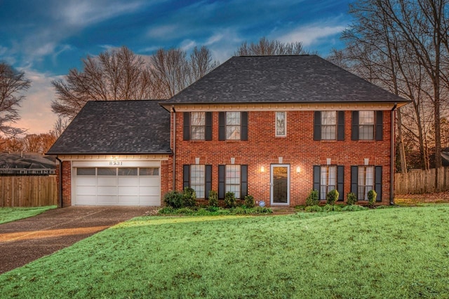 colonial inspired home featuring a shingled roof, brick siding, fence, and an attached garage