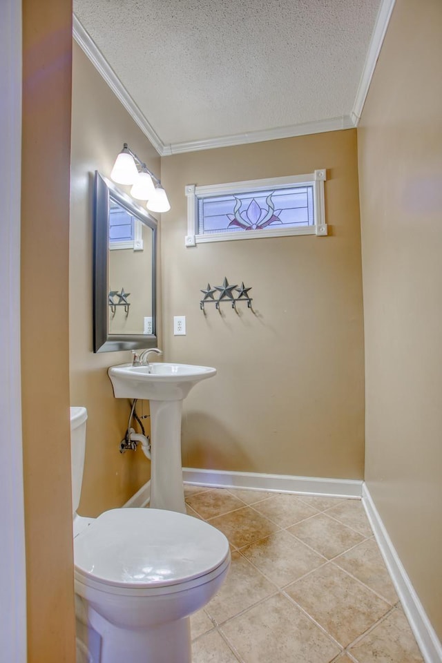 bathroom with crown molding, toilet, a textured ceiling, tile patterned flooring, and baseboards