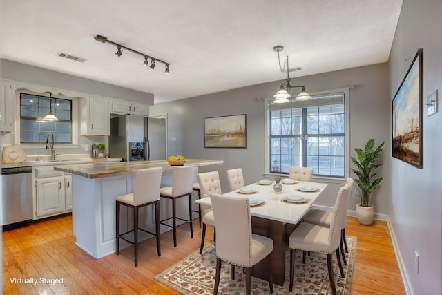 dining room featuring light wood finished floors, baseboards, visible vents, and track lighting