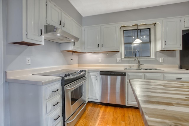 kitchen featuring light wood-style floors, appliances with stainless steel finishes, under cabinet range hood, white cabinetry, and a sink