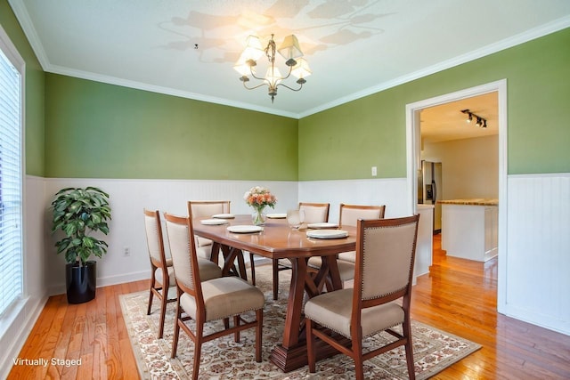 dining space with light wood-style flooring, ornamental molding, a notable chandelier, and wainscoting