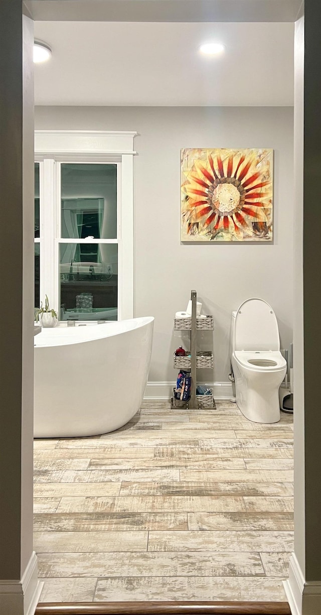 bathroom featuring a freestanding bath, baseboards, and wood finished floors