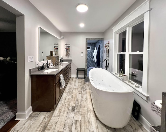 full bathroom featuring double vanity, a soaking tub, a sink, and wood finished floors