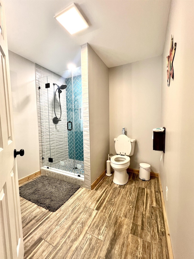 bathroom with baseboards, wood finished floors, toilet, and a shower stall