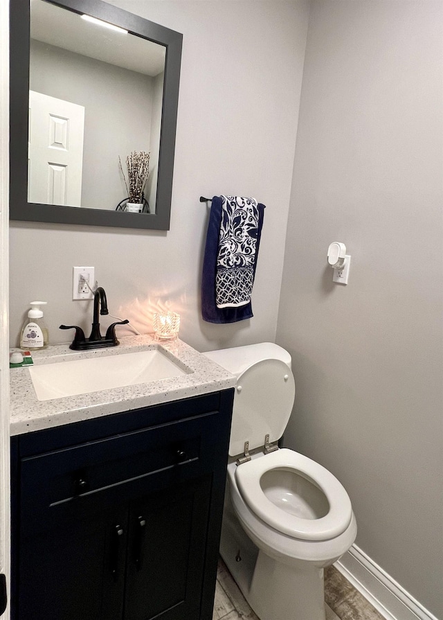 half bathroom featuring toilet, vanity, and baseboards