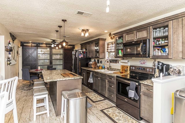 kitchen featuring a barn door, a sink, visible vents, a center island, and black appliances