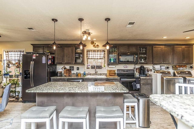 kitchen with dark brown cabinetry, stainless steel appliances, a kitchen island, a sink, and washer and dryer