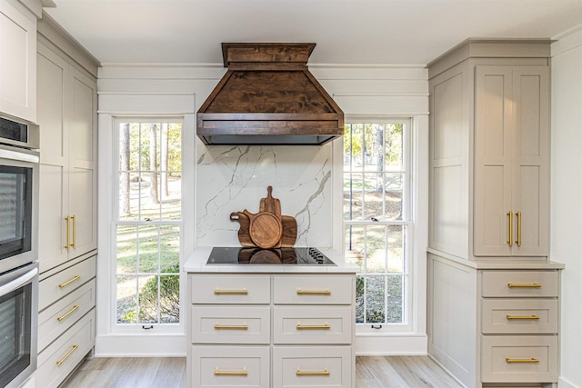 kitchen with premium range hood, light wood-style floors, black electric cooktop, and tasteful backsplash