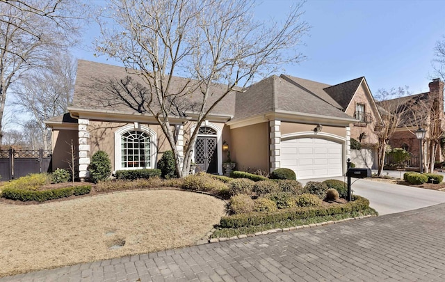 view of front of home featuring an attached garage, a shingled roof, fence, driveway, and stucco siding