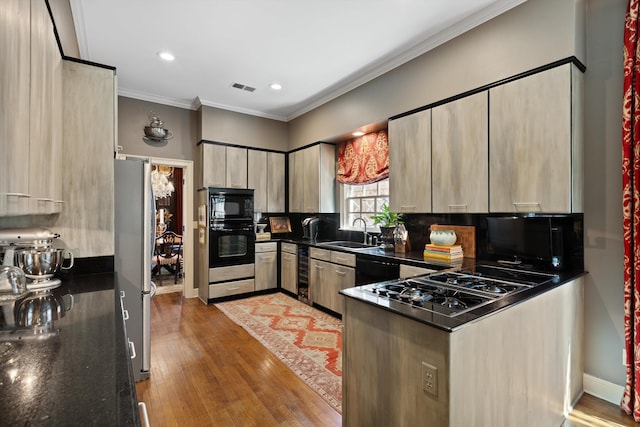 kitchen featuring visible vents, hardwood / wood-style flooring, ornamental molding, black appliances, and a sink