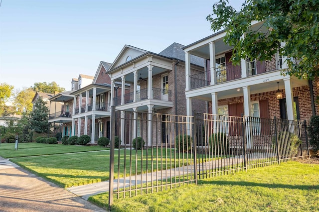 greek revival inspired property featuring fence, a front lawn, a ceiling fan, and brick siding