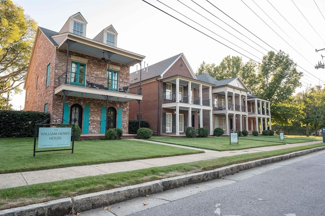 view of front of house featuring a balcony, a front lawn, and brick siding