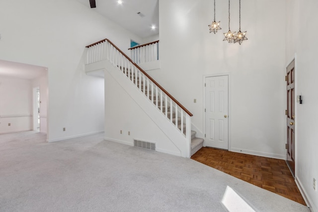 foyer entrance featuring visible vents, stairway, a high ceiling, a chandelier, and baseboards