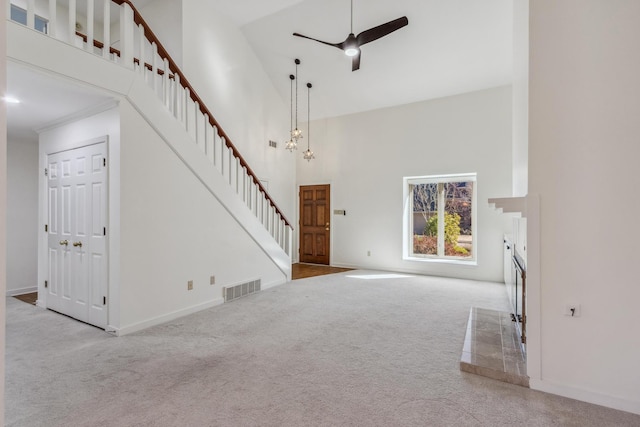 unfurnished living room with stairs, visible vents, a towering ceiling, carpet flooring, and ceiling fan with notable chandelier