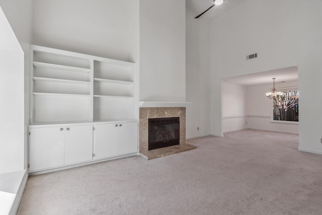 unfurnished living room featuring carpet floors, a fireplace, visible vents, a towering ceiling, and a chandelier