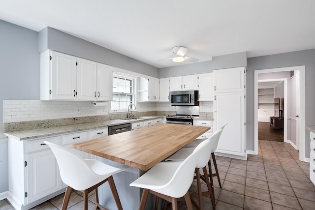 kitchen featuring a kitchen island, a sink, white cabinetry, appliances with stainless steel finishes, and decorative backsplash