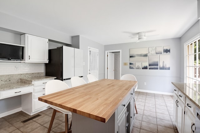 kitchen with light tile patterned floors, a ceiling fan, a kitchen breakfast bar, white cabinets, and tasteful backsplash