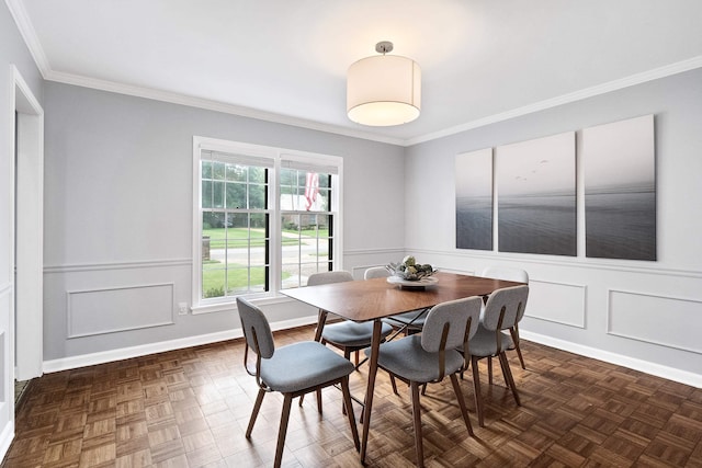 dining room featuring crown molding, a wainscoted wall, baseboards, and a decorative wall