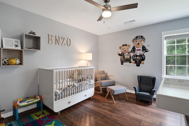 bedroom with a crib, baseboards, visible vents, a ceiling fan, and wood finished floors