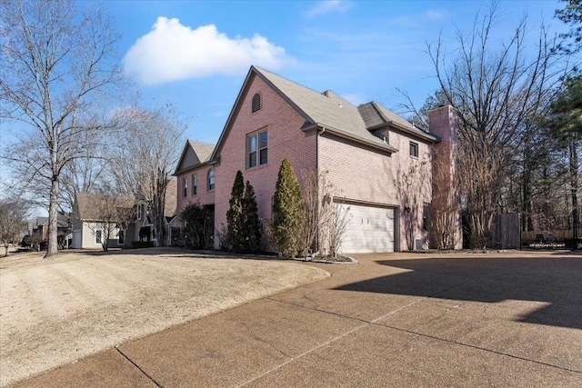 view of property exterior with an attached garage, driveway, a chimney, and brick siding