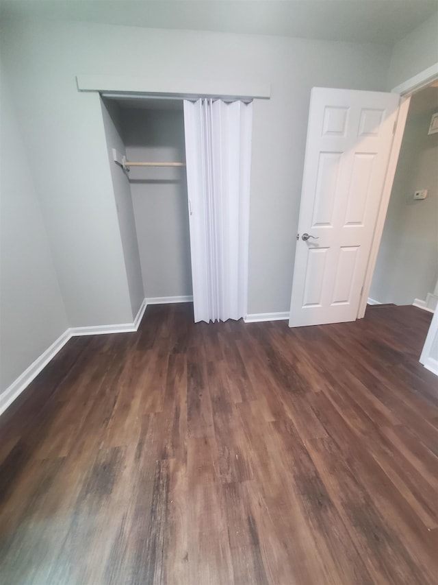 unfurnished bedroom with dark wood-style floors, baseboards, and a closet