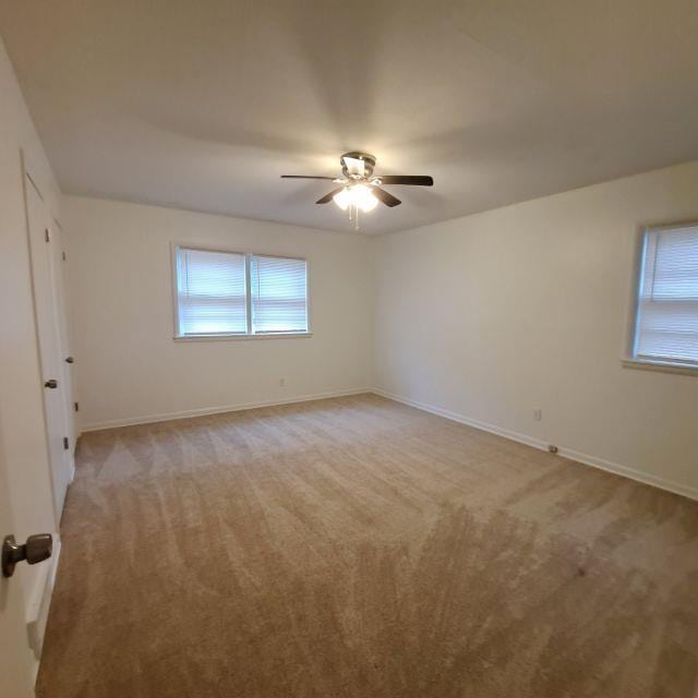 spare room with light colored carpet, baseboards, and a ceiling fan