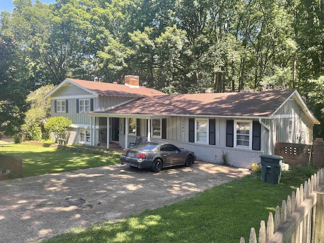 split level home featuring board and batten siding, driveway, a front lawn, brick siding, and a chimney