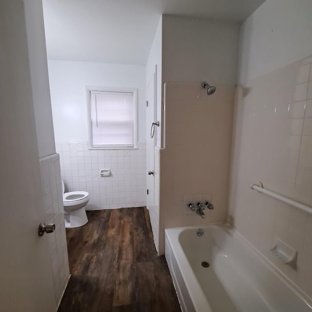 full bath with a wainscoted wall, bathtub / shower combination, toilet, wood finished floors, and tile walls
