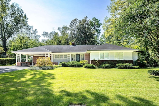 ranch-style house featuring brick siding, a chimney, an attached carport, driveway, and a front lawn