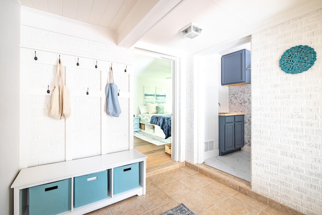 mudroom with crown molding, light tile patterned floors, visible vents, brick wall, and beamed ceiling