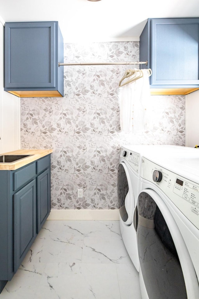 clothes washing area featuring cabinet space, wallpapered walls, marble finish floor, washing machine and dryer, and a sink