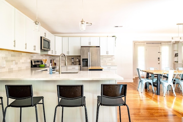 kitchen with white cabinets, a peninsula, stainless steel appliances, light wood-style floors, and backsplash