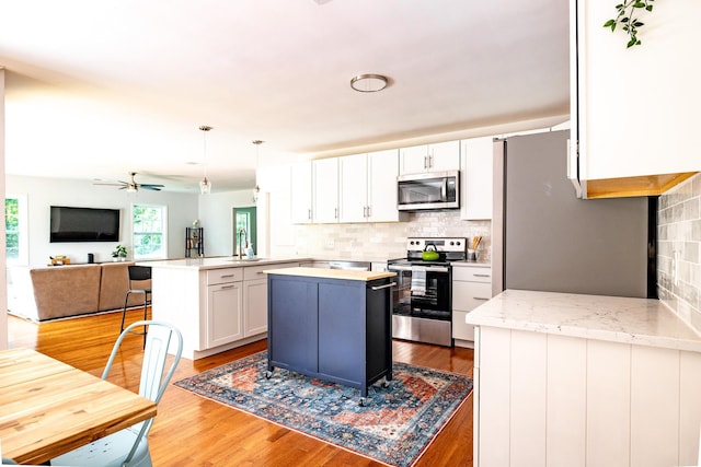 kitchen with a peninsula, light wood finished floors, appliances with stainless steel finishes, and white cabinets