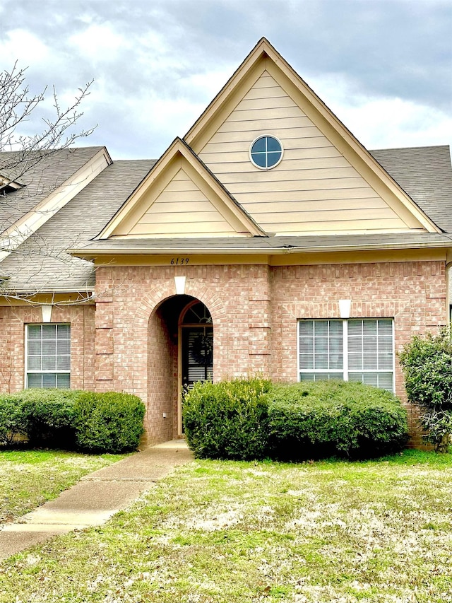 view of front of property featuring a front yard, brick siding, and roof with shingles