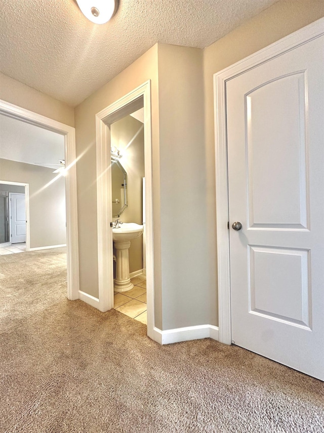 corridor featuring a textured ceiling, carpet flooring, and baseboards