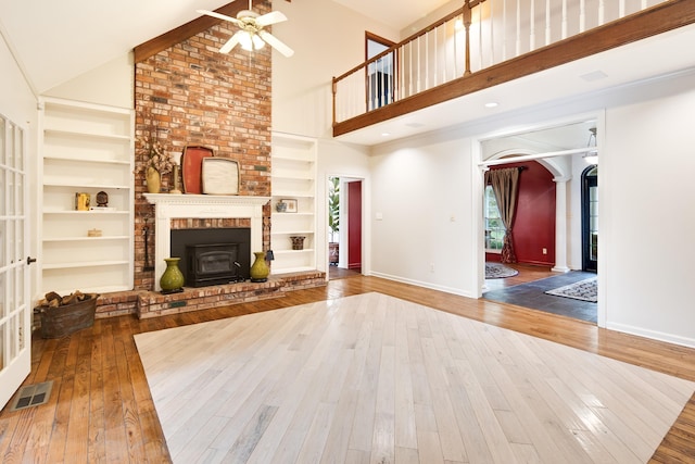 unfurnished living room featuring arched walkways, built in shelves, wood-type flooring, and visible vents