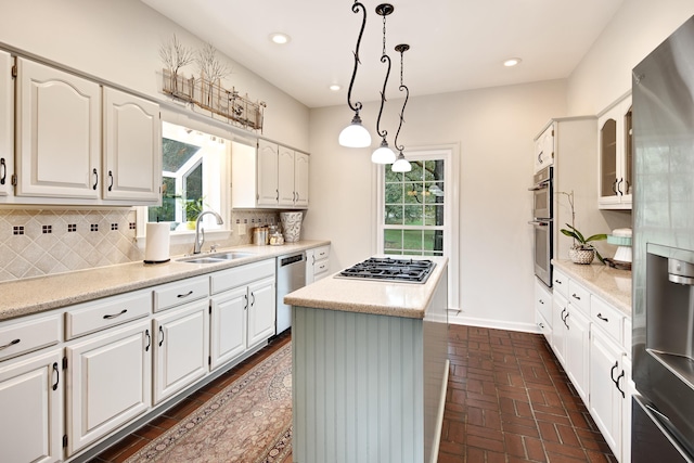 kitchen featuring brick floor, a kitchen island, a sink, white cabinets, and backsplash