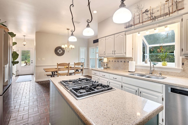 kitchen featuring brick floor, stainless steel appliances, backsplash, white cabinetry, and a sink