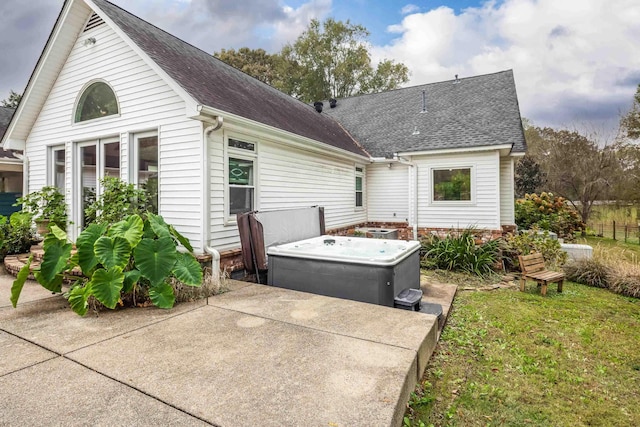 rear view of house with roof with shingles, a patio, and a hot tub