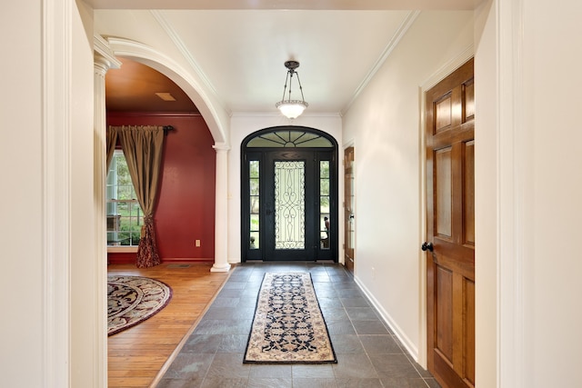 foyer entrance with decorative columns, crown molding, arched walkways, and baseboards